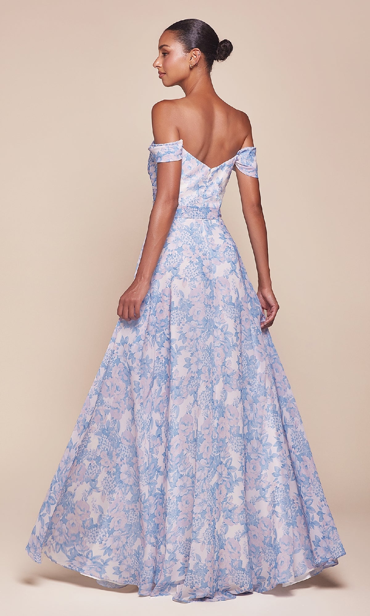 A woman stands with her back to the camera in the elegant and affordable Ladivine 7441 Long Floral-Print A-Line Prom Dress—a light blue, off-the-shoulder gown perfect for any special occasion—against a plain beige background.
